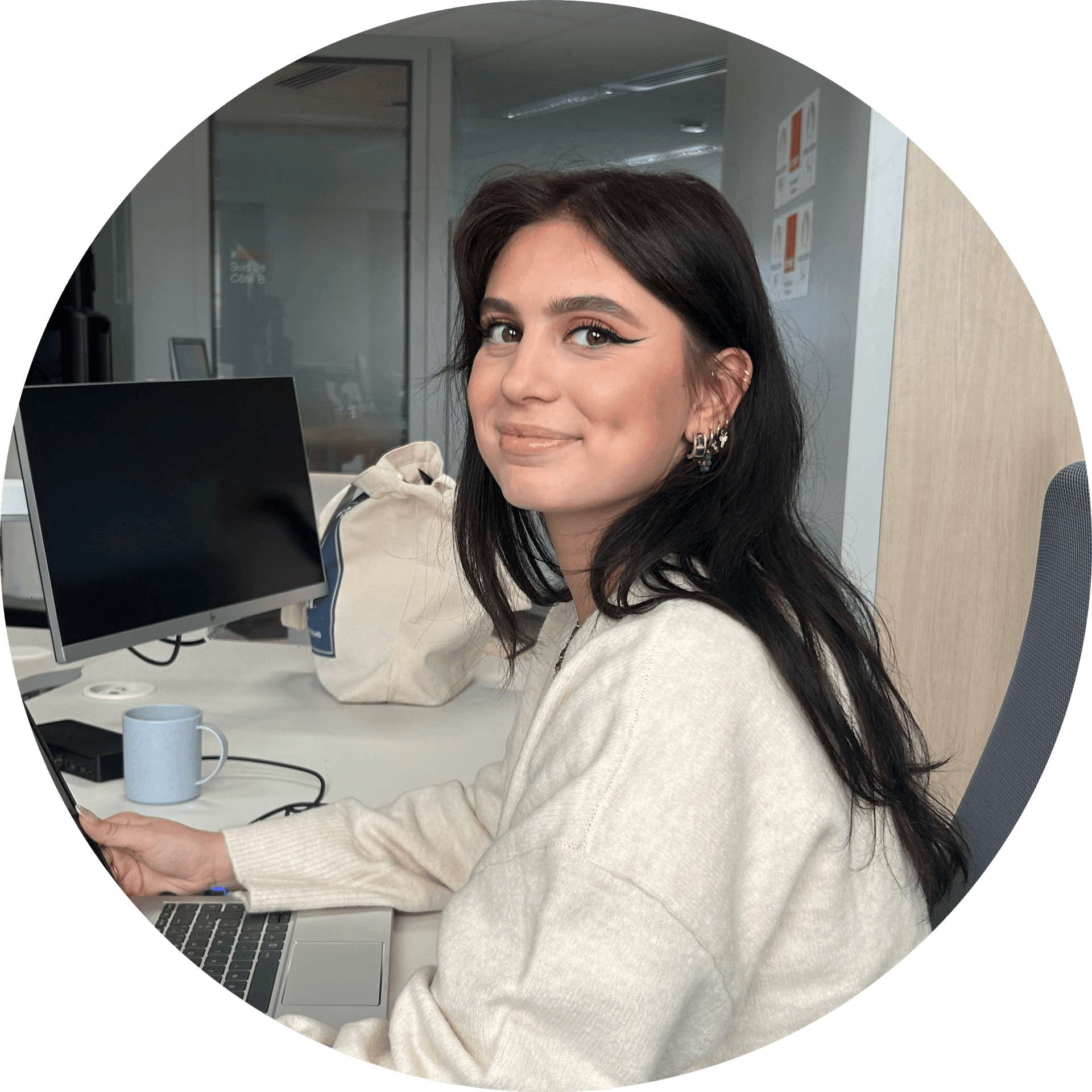 Woman smiling at desk with computer in an office, wearing a cream sweater.