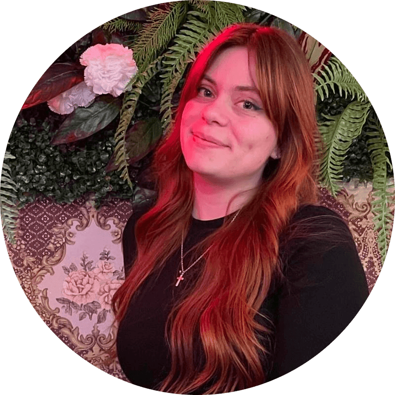 Woman with long hair smiling in front of a floral and leafy background.